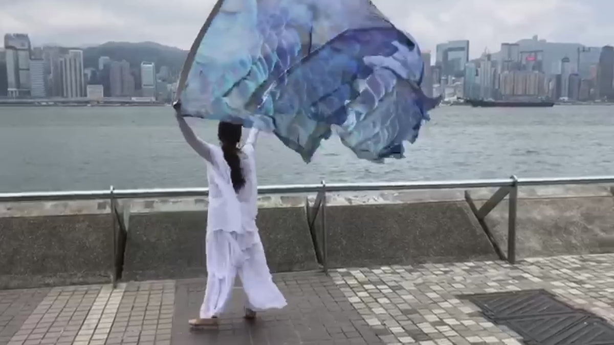 Under His Wings Psalm 91 silk worship flags demonstrated in expressive worship movement.  Woman worshipping with Under His Wings Psalm 91 silk worship flags with Hong Kong skyline in background