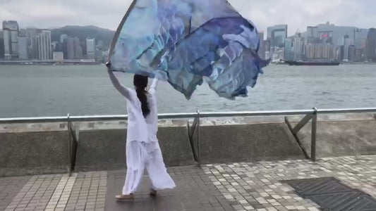Under His Wings Psalm 91 silk worship flags demonstrated in expressive worship movement.  Woman worshipping with Under His Wings Psalm 91 silk worship flags with Hong Kong skyline in background
